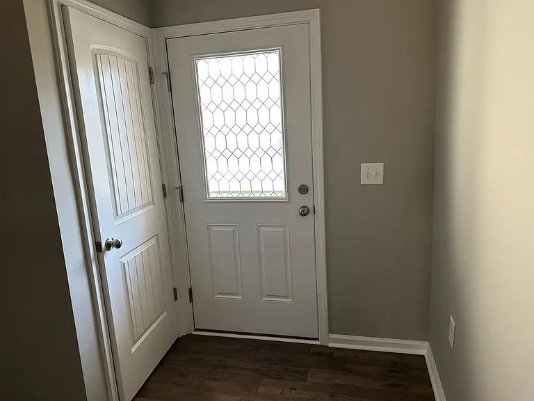 A view of the front door, and the coat closet. Behind you is the living area and to the left are the stairs.