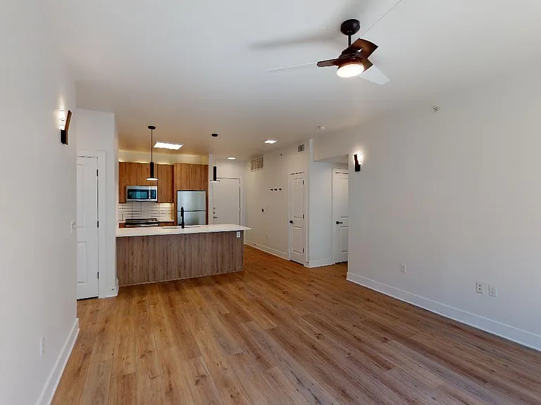 Apartment kitchen with stainless steel appliances, dining and living room with wood-style flooring.