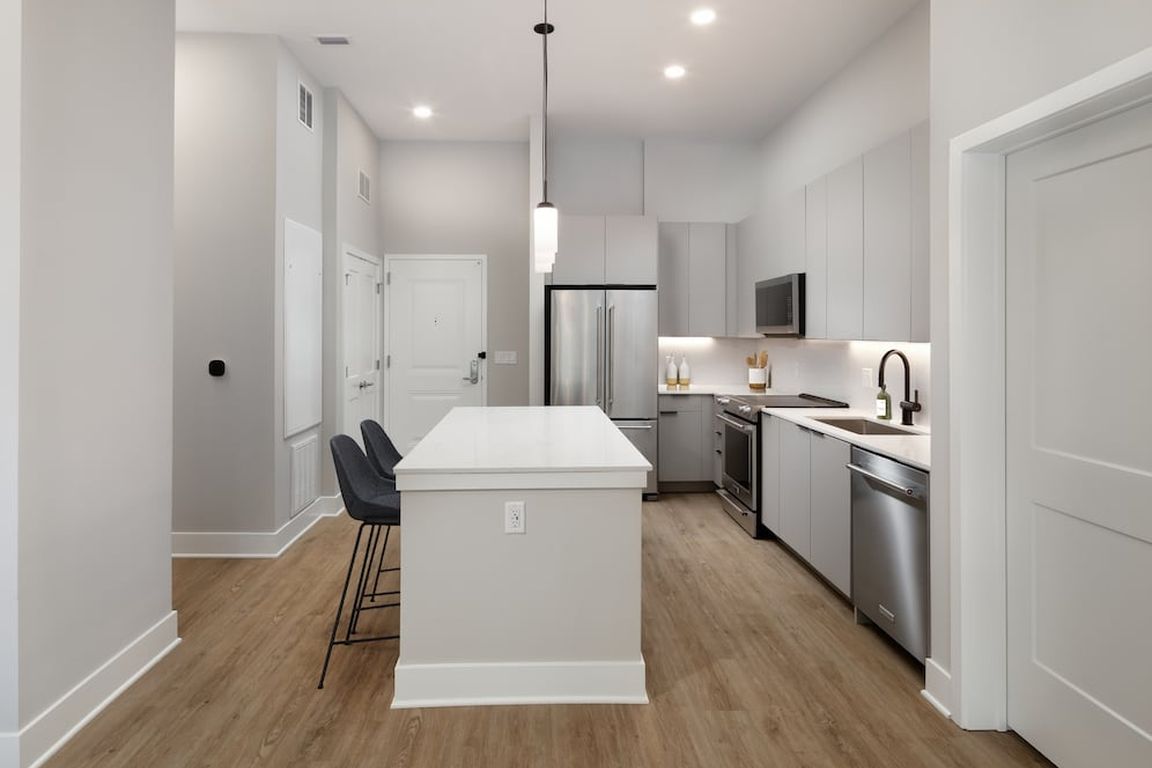 Signature Collection kitchen with stainless steel appliances, light grey cabinetry, marbled quartz countertops and backsplash, under-cabinet lighting, and hard-surface flooring