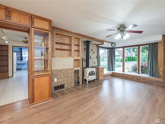 The spacious living room features planked laminate flooring, custom built-ins, a free-standing wood stove, a ceiling fan/light, and tile walls.  The large wrap-around windows provide excellent natural lighting.