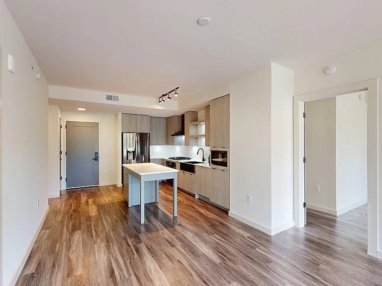 Apartment kitchen with black stainless steel appliances, dining and living room with wood-style flooring.
