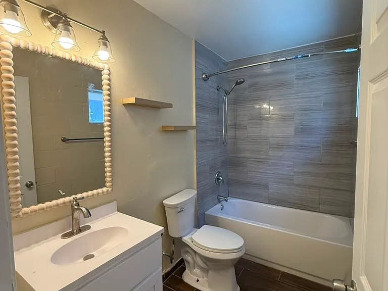 The bathroom has a full bathtub, new fixtures, tile flooring, and floating shelves.