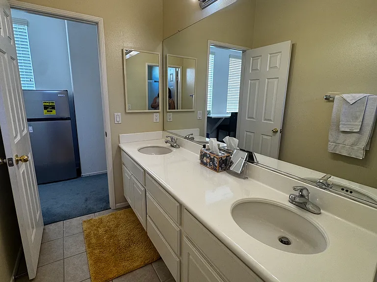 Shared bathroom for two tenants with tile floor, rugs, two sinks, lighting, spacious and comfortable