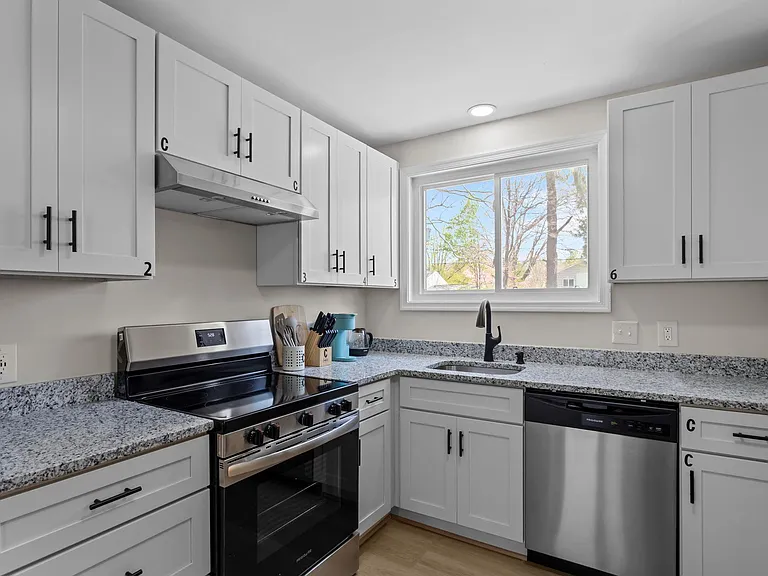 Main community kitchen, with electric stove, dishwasher, bowls, plates, cups, mugs, eating utensils