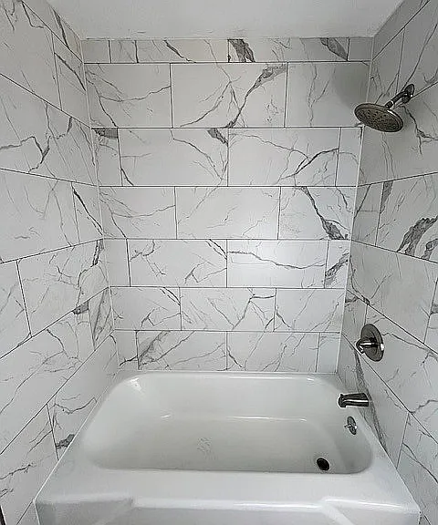 Elegant bathroom showcasing luxurious marble tile walls and a modern bathtub with a sleek showerhead.