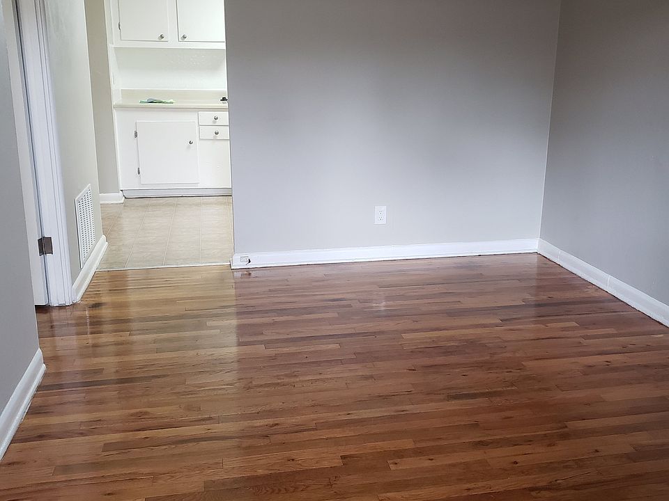 Charming room with gleaming hardwood floors leading to a bright kitchen with white cabinetry.