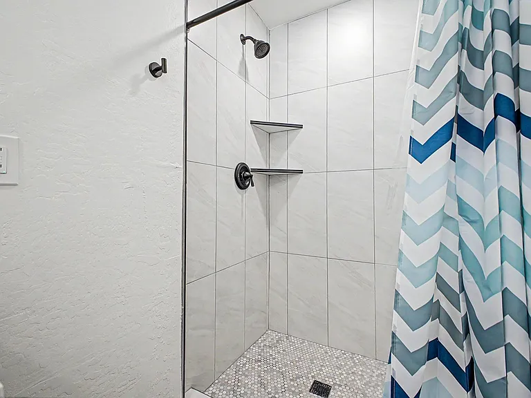 Walk-in tiled shower with rainfall-style head, corner shelving for toiletries, and pebble-look mosaic flooring.