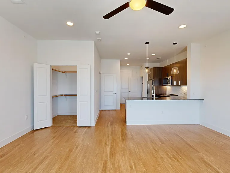 Apartment kitchen with stainless steel appliances, dining and living room with wood-style flooring.