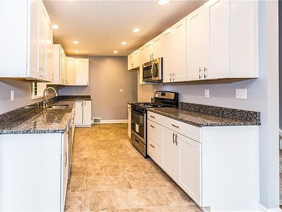 Galley style kitchen has plenty of crisp new white cabinetry & granite counter tops for storing ingredients & preparing gourmet 