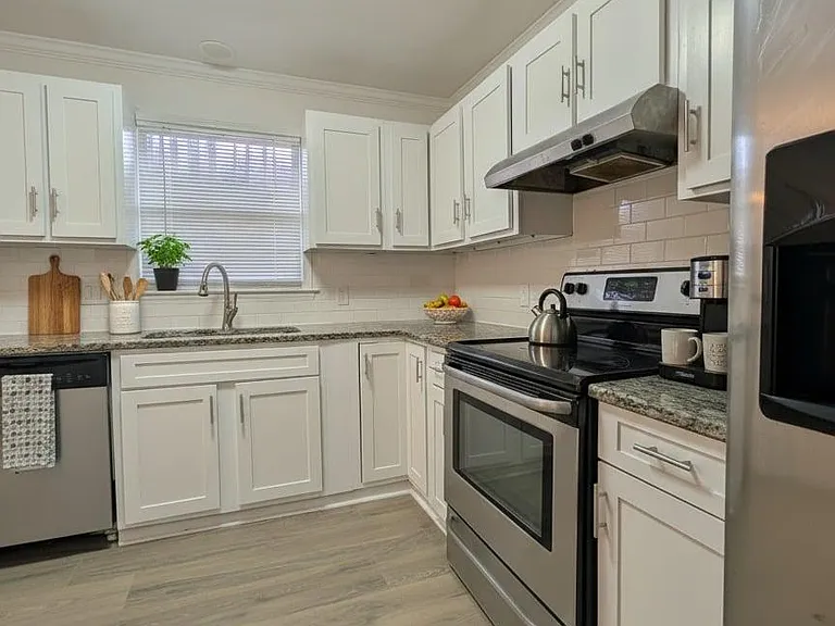 U-shaped kitchen with ample white cabinetry, granite-look counters, subway-tile backsplash, and stainless appliances.