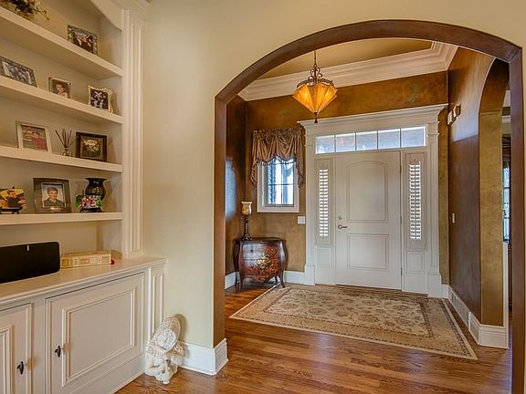 Warm and welcoming foyer with light from transom & sidelights, deep crown trim, coppery bronze walls and romantic ceiling fixture.