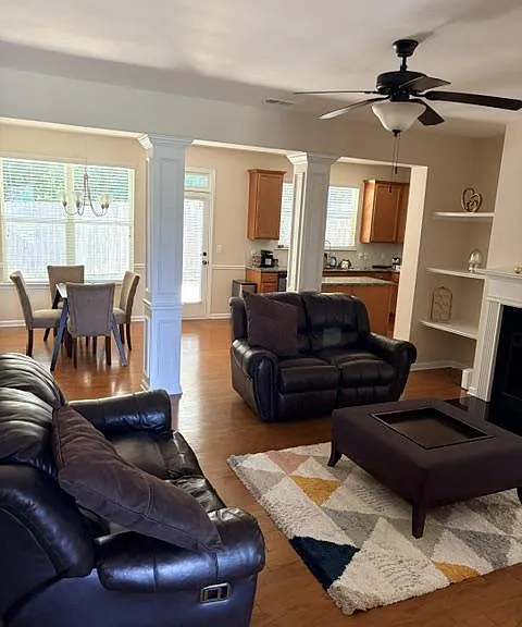 Open-concept living area with leather seating, ceiling fan, and fireplace, flowing into a dining nook and kitchen.