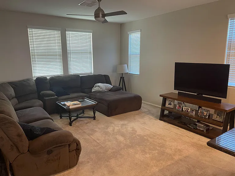 Spacious living room with plush sectional seating, ceiling fan, and multiple windows with blinds for comfortable everyday lou