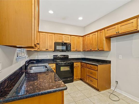 Kitchen featuring black appliances, light tile patterned floors, sink, and dark stone counters