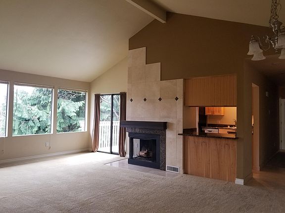 Large living/dining room with vaulted ceiling, large windows, wood burning fireplace & access to deck