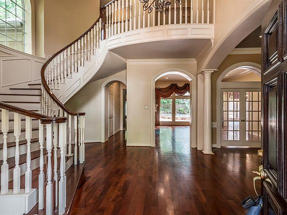 Classic entry features a curved staircase, rich wood flooring. Arched doorways are elegant.