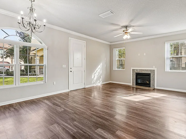 Inviting living room with elegant chandelier, large sunlit windows, and cozy fireplace, featuring sleek hardwood flooring.