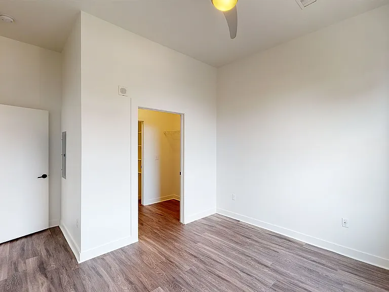 Spacious apartment bedroom with large closet, attached bathroom and wood-style flooring.