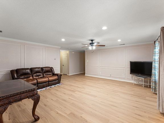 Spacious living area featuring light wood-finish flooring, decorative wall paneling, and a contemporary ceiling fan