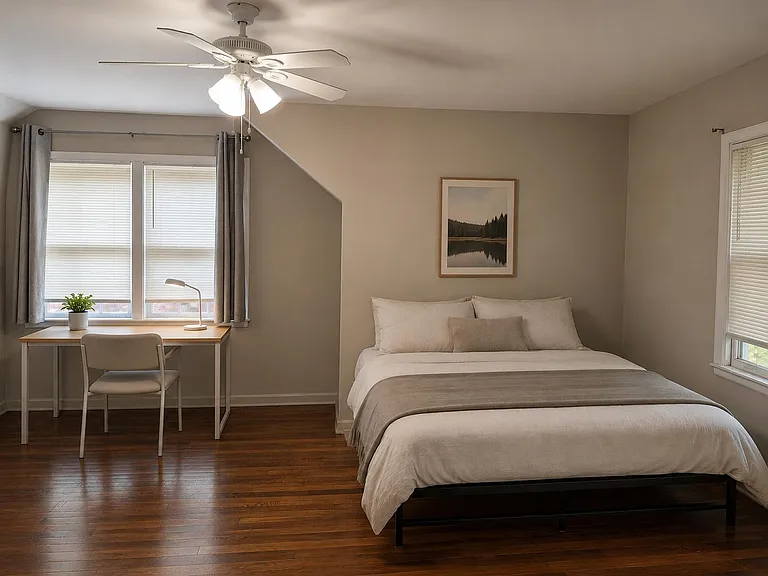 Well-appointed bedroom with hardwood floors, ceiling fan, two windows, and a dedicated desk workspace for studying or remote