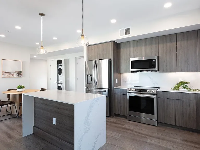 Signature Collection Kitchen with wood cabinetry, marbled quartz countertop and backsplash, upgraded stainless steel appliances, and hard surface flooring