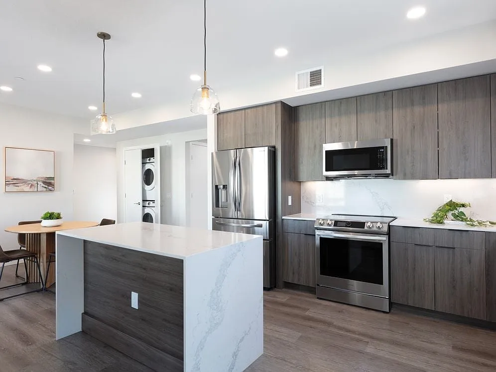 Signature Collection Kitchen with wood cabinetry, marbled quartz countertop and backsplash, upgraded stainless steel appliances, and hard surface flooring - Avalon West Dublin