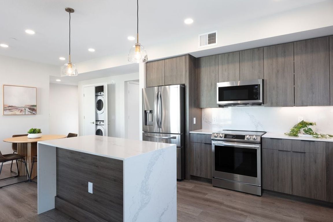 Signature Collection Kitchen with wood cabinetry, marbled quartz countertop and backsplash, upgraded stainless steel appliances, and hard surface flooring
