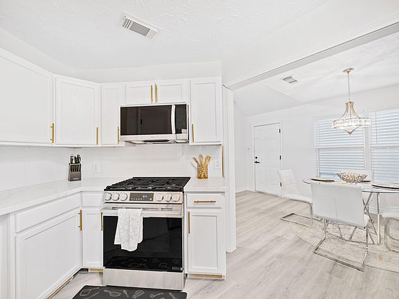 Updated kitchen with white cabinetry, ample counter space, and a gas range with over-the-range microwave, plus adjacent dinin
