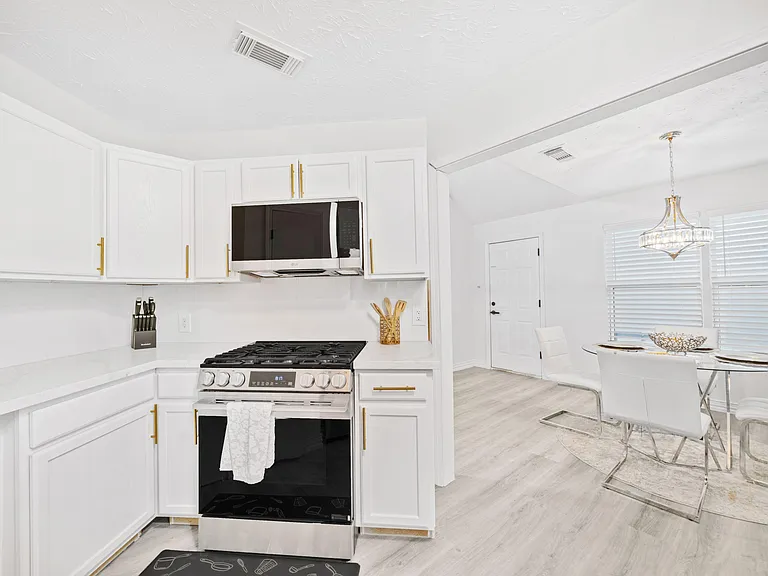 Updated kitchen with white cabinetry, ample counter space, and a gas range with over-the-range microwave, plus adjacent dinin
