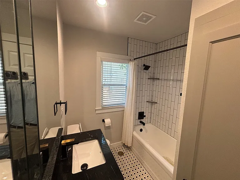 Bathroom featuring a black countertop vanity with a rectangular sink, wall-mounted faucet, and an adjacent built-in bathtub with subway tile surround and matte black fixtures