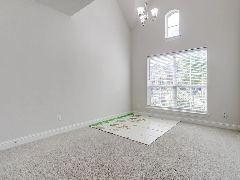 Carpeted spare room featuring high vaulted ceiling and a notable chandelier