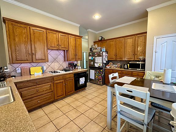 Kitchen featuring wood cabinets, black appliances, gas cooktop, ornamental molding, light tile patterned flooring, and light countertops