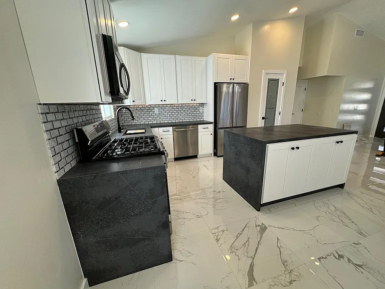 Kitchen with new SS appliances, quartz countertops, white shaker cabinets, workstation sink, island and under cabinet lighting.