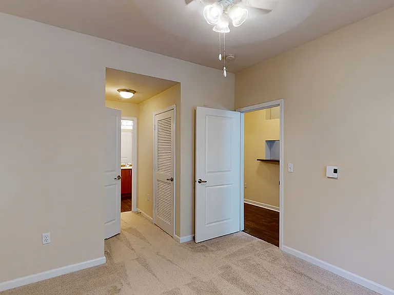 Spacious apartment bedroom with large closet, attached bathroom and plush carpet flooring.