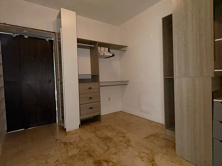 Bedroom area with marble-look flooring and a built-in closet system featuring drawers, shelving, and hanging space.