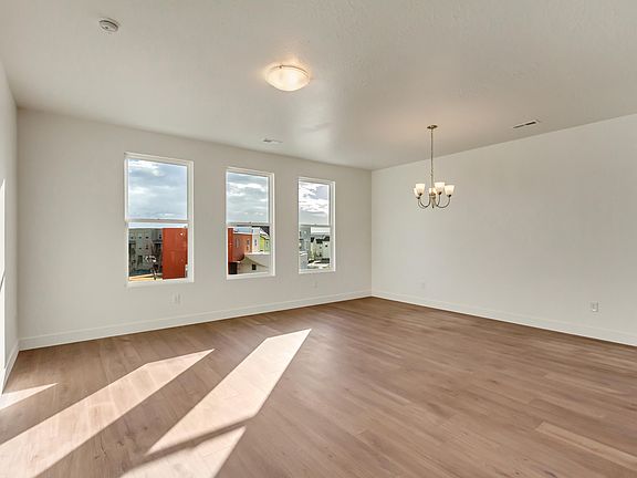 Empty room with wood flooring, three large windows, and a ceiling light. A chandelier is in the corn