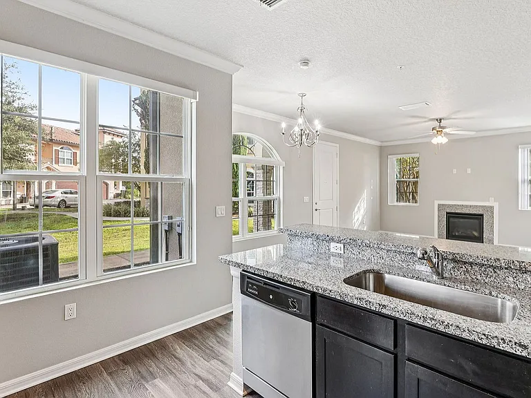 Bright and inviting living area with stylish granite countertops, modern chandelier, and large windows overlooking a serene neighborhood view.