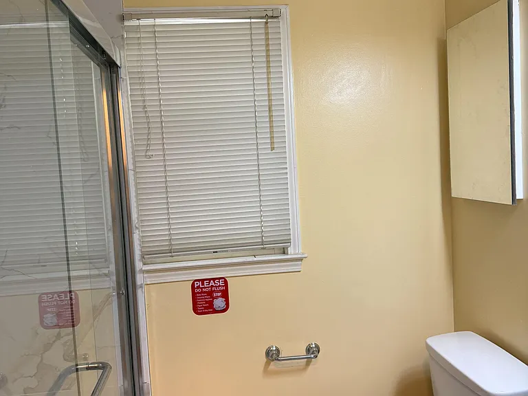 Bathroom with glass-enclosed tub/shower, window with blinds, and vanity countertop for daily essentials.