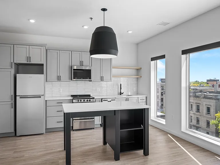 Modern kitchen with sleek gray cabinetry, stainless steel appliances, and large windows offering a bright city view. Modern kitchen with sleek gray cabinetry, stainless steel appliances, and large windows offering a bright city view.