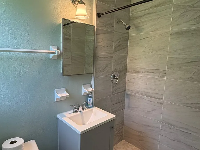 Updated bathroom with a tiled walk-in shower, compact vanity with storage, and wall-mounted mirror and lighting.