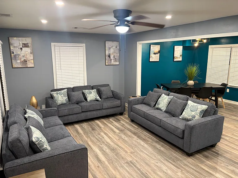 Spacious shared living room with multiple sofas, ceiling fan lighting, and an open connection to the dining area.