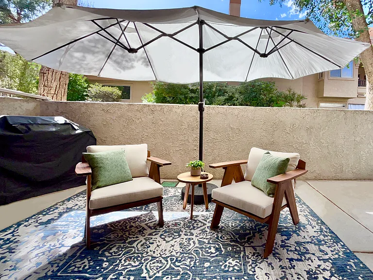 Experience the luxurious outdoor living area, featuring premium lounge chairs with a large umbrella, a propane BBQ, and serene privacy surrounded by lush trees perfect for relaxation and entertaining in style.