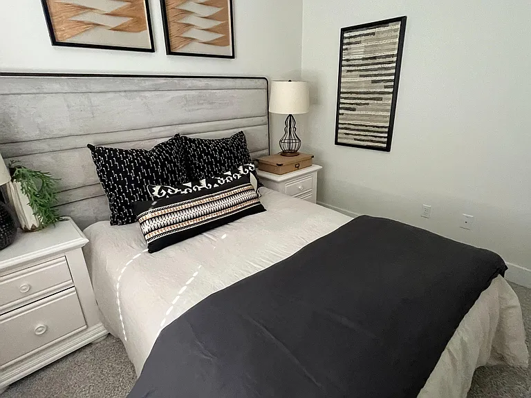 Furnished bedroom with a full bed, nightstand lighting, and carpeted floors, accented by wall art for a finished feel.
