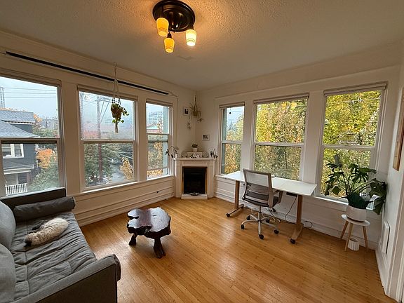 SW facing living room with 6 big windows with hillside views, a gas fireplace, an adjustable desk, a pull-out sofa for guests, a wood slab coffee table, an adjustable side table, with french doors to the bedroom. (cat not included)