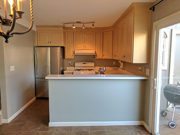 Open kitchen with stainless fridge, dishwasher, and microwave plus a white stove. Breakfast bar overlooks the living area. Sliding doors add light and lead to the private patio, with stairs to the upper level.