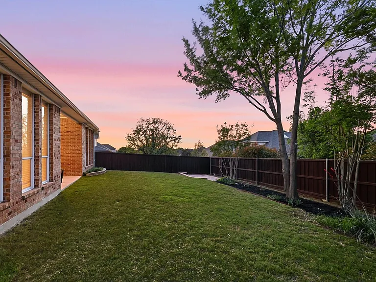 Expansive backyard featuring a lush lawn, mature trees, and a privacy fence