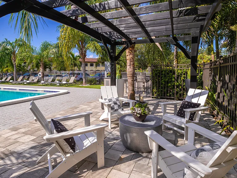 Relax in the comfortable, shaded poolside lounge featuring cozy seating under a pergola and views of the sparkling pool.