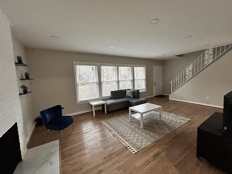 Open living room with hardwood floors, large windows, and comfortable seating area near the entry and staircase.