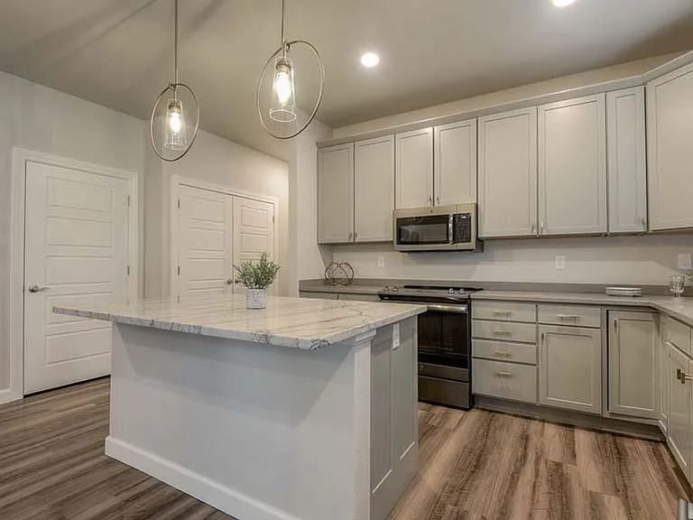 The Cardiff- Spacious Kitchen w/Large Natural Quartzite Center Island. Includes a Generously Sized Pantry Closet and Conveniently Placed Laundry Closet at Left Leading Towards Back 2 Bedrooms