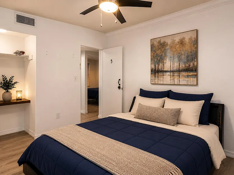 Furnished bedroom with a queen bed, ceiling fan, and built-in open shelving for easy everyday storage.